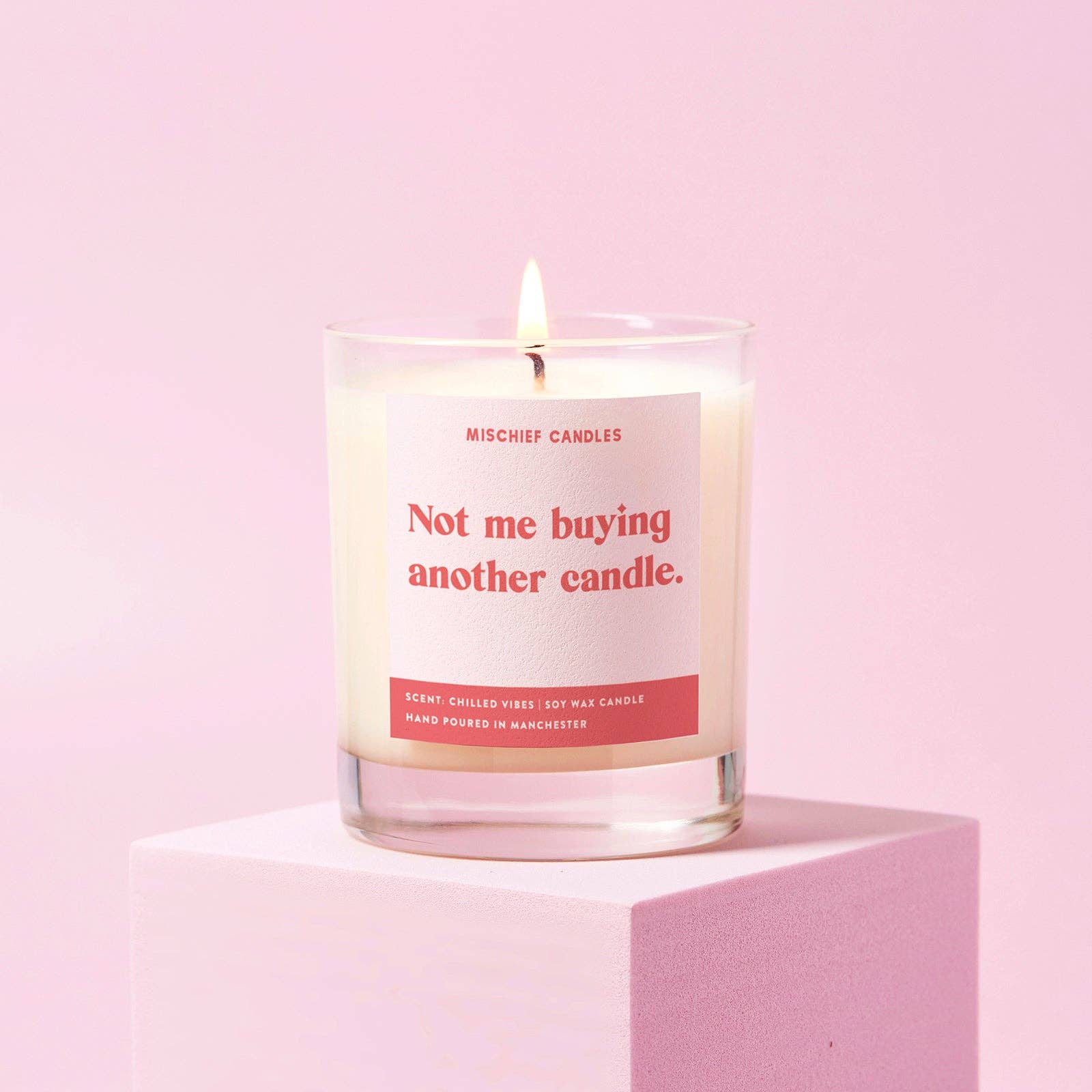 Candle with a humorous label ' not me buying another candle' on a pink background