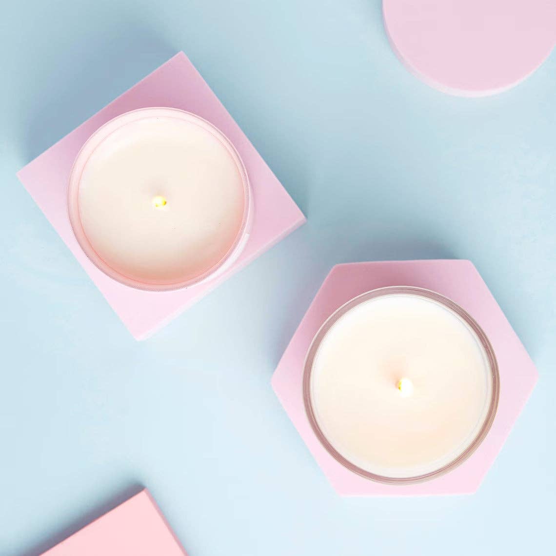 Two white candles in pink holders on a light blue background.