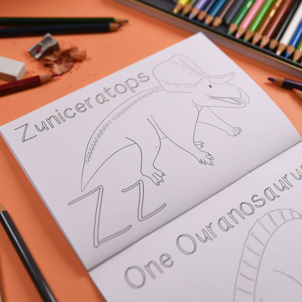 Colouring book with dinosaur illustrations and coloring pencils on an orange surface