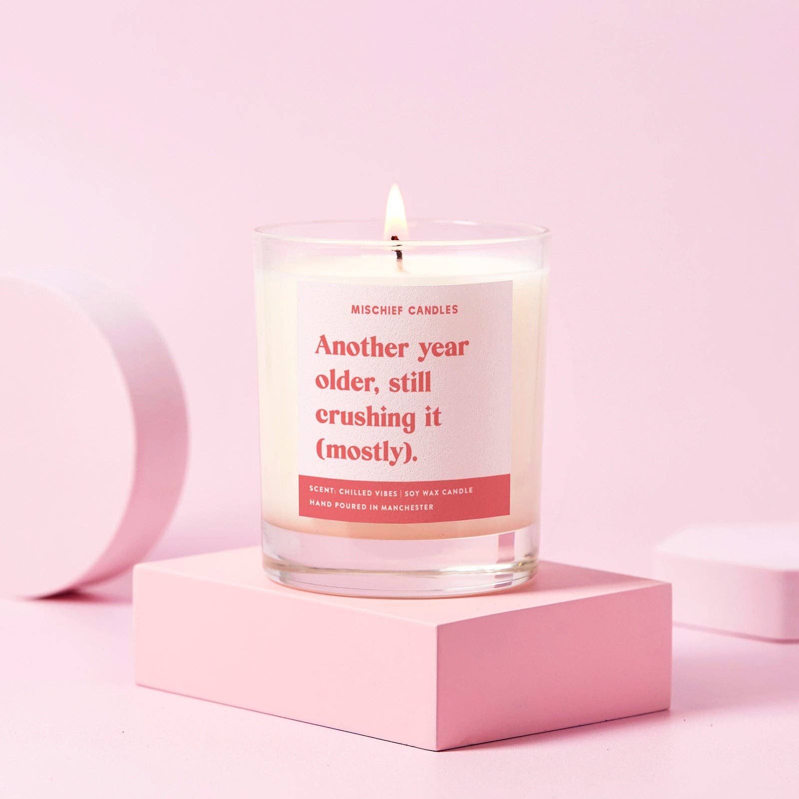 Candle in clear glass jar with label saying another year older, still crushing it (mostly)