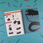Notebook with bat illustration and craft instructions on a blue background with colorful sticks.