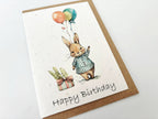 Birthday card with a rabbit holding balloons and the text 'Happy Birthday' on a white background.